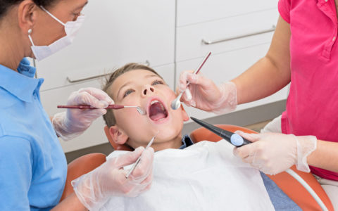 Junge liegt mit offenem Mund auf Zahnarztstuhl bei Untersuchung