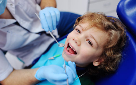 lächelndes Kind sitzt auf einem blauen Stuhl Zahnarzt