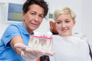 Zahnärztin zeigt Patientin ein Zahnimplantat. 