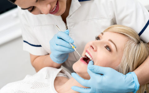 Zahnärztin untersucht Zähne mit Spiegel in der Klinik