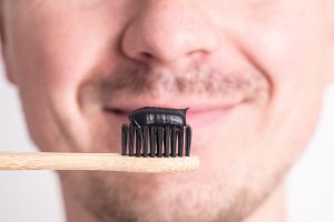 Lächelnder Mann hält eine Zahnbürste mit Aktivkohle-Zahnpasta darauf