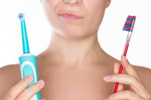Young beautiful woman undecided whether to use the electric or traditional toothbrush, isolated over a white background