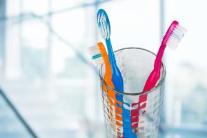 New colorful toothbrushes in a glass on blur background