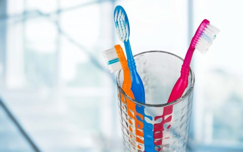 Neue bunte Zahnbürsten in einem Glas auf verschwommenem Hintergrund
