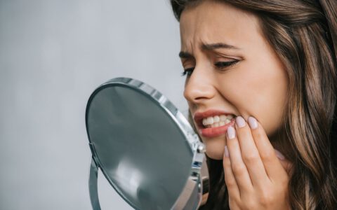Nahaufnahme einer jungen Frau, die Zahnschmerzen hat und in den Spiegel schaut