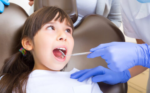 Kind beim Zahnarzt mit offenen Mund eine eine Zahnarzt Helferin die ein Instrument in ihr Mund hält