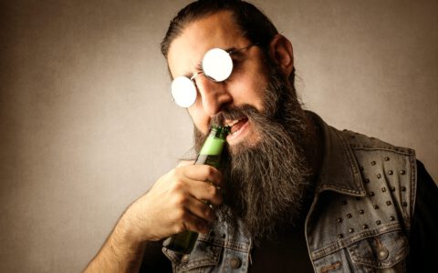 bärtiger Mann öffnet Bier mit Zähnen