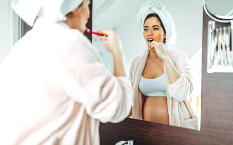 schwangere Frau putz sich die Zähne im Spielgel