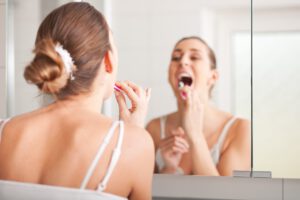 Junge Frau putzt sich die Zähne vor dem Spiegel