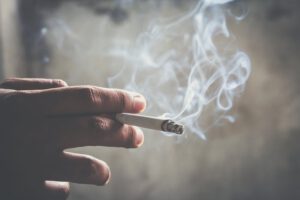Mann hält rauchend eine Zigarette in der Hand. Zigarettenrauch verbreitet. dunklen Hintergrund