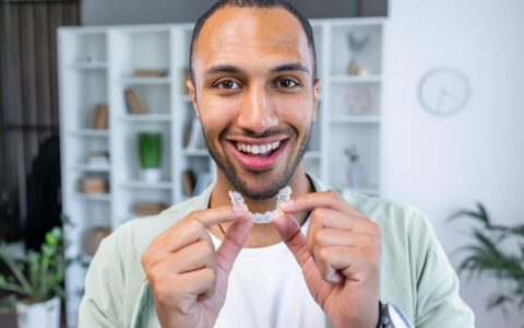 Erwachsener Mann, der eine durchsichtige Zahnspange zur Zahnkorrektur einsetzt und einen unsichtbaren kieferorthopädischen Retainer und Aligner hält. Kunststoffspange Zahnmedizin zur Zahnkorrektur